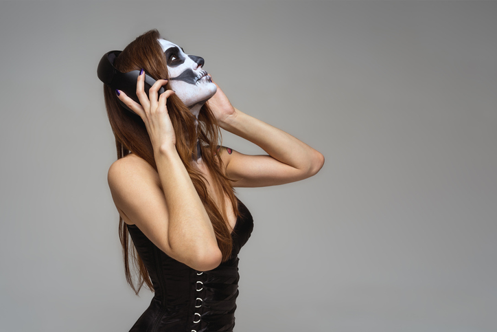 Portrait of young beautiful girl with fearful halloween skeleton makeup  Katrina Calavera in headphones listening to music on gray background