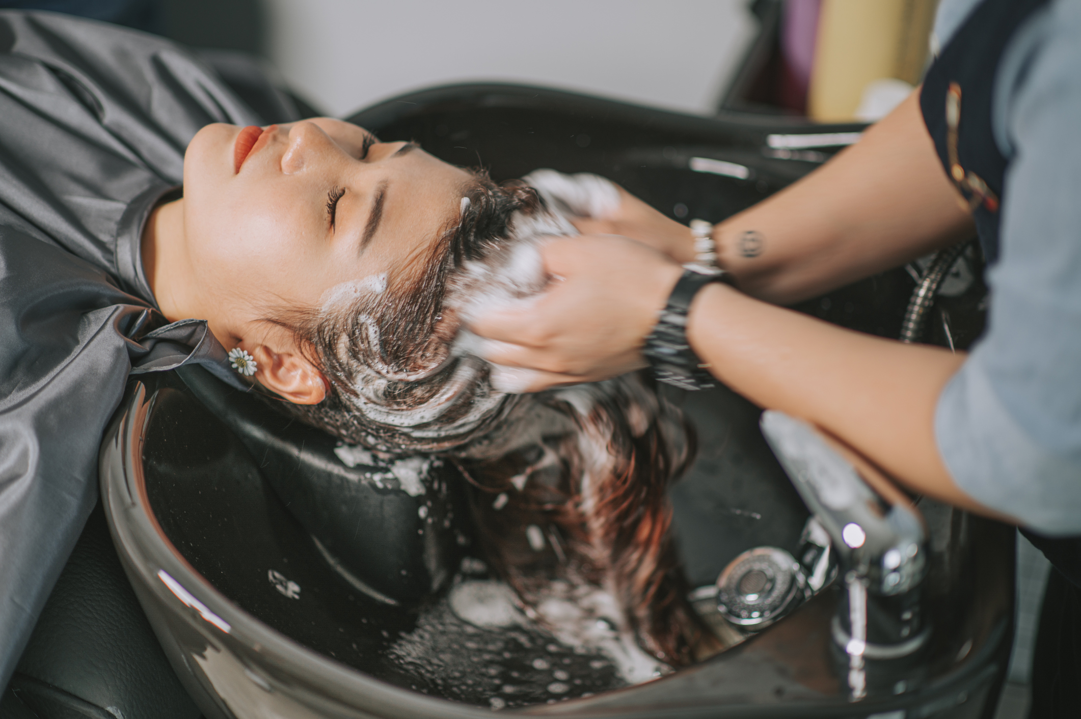 Directly above Asian chinese female lying down for hair wash at hair salon with eyes closed